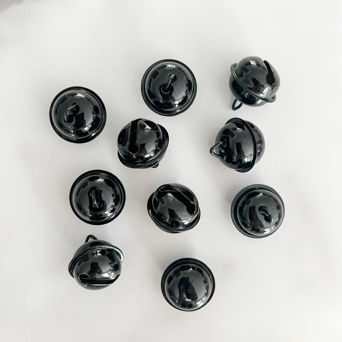 Ten small glossy black jingle bells arranged in a loose circle on a light white marble surface.