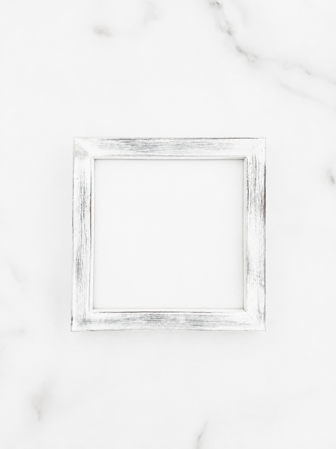 A small 5 inch by 5 inch square picture frame with a distressed white and gray painted finish, centered on a light marble background.