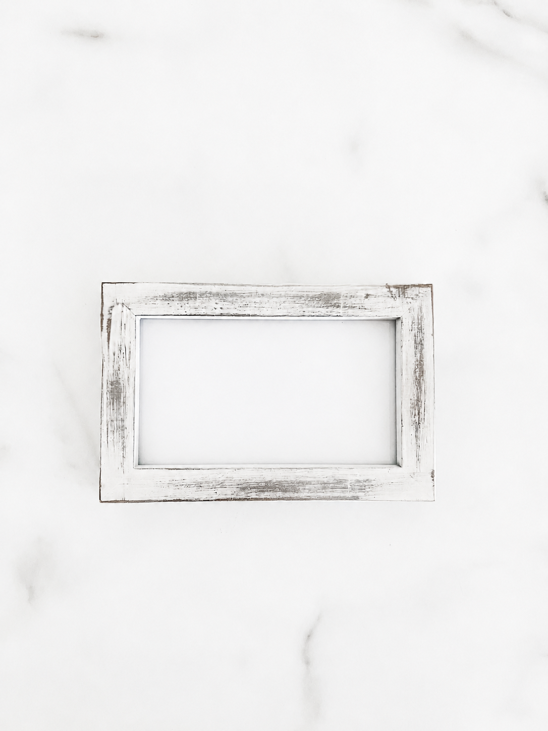 A small 5 inch by 3 inch square picture frame with a distressed white and gray painted finish, centered on a light marble background.