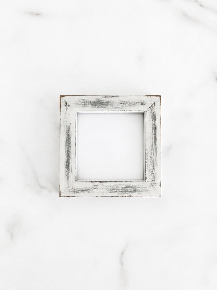 A small 4 inch by 4 inch square picture frame with a distressed white and gray painted finish, centered on a light marble background.