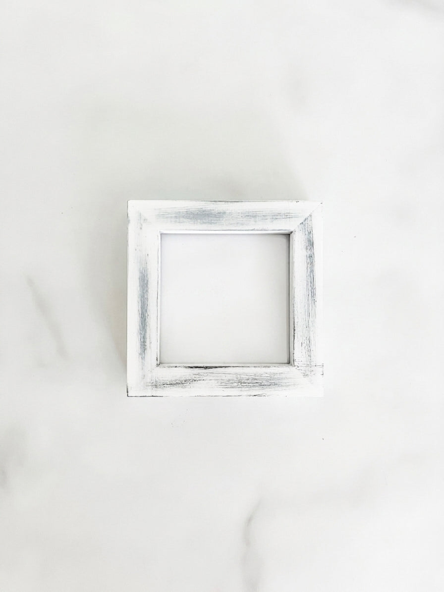 A small 3 inch by 3 inch square picture frame with a distressed white and gray painted finish, centered on a light marble background.