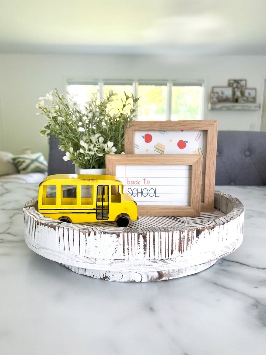 Metal yellow school bus lazy susan decor, back to school decoration and classroom decor shown on a white lazy susan with two wood framed back to school signs and some floral arrangement.