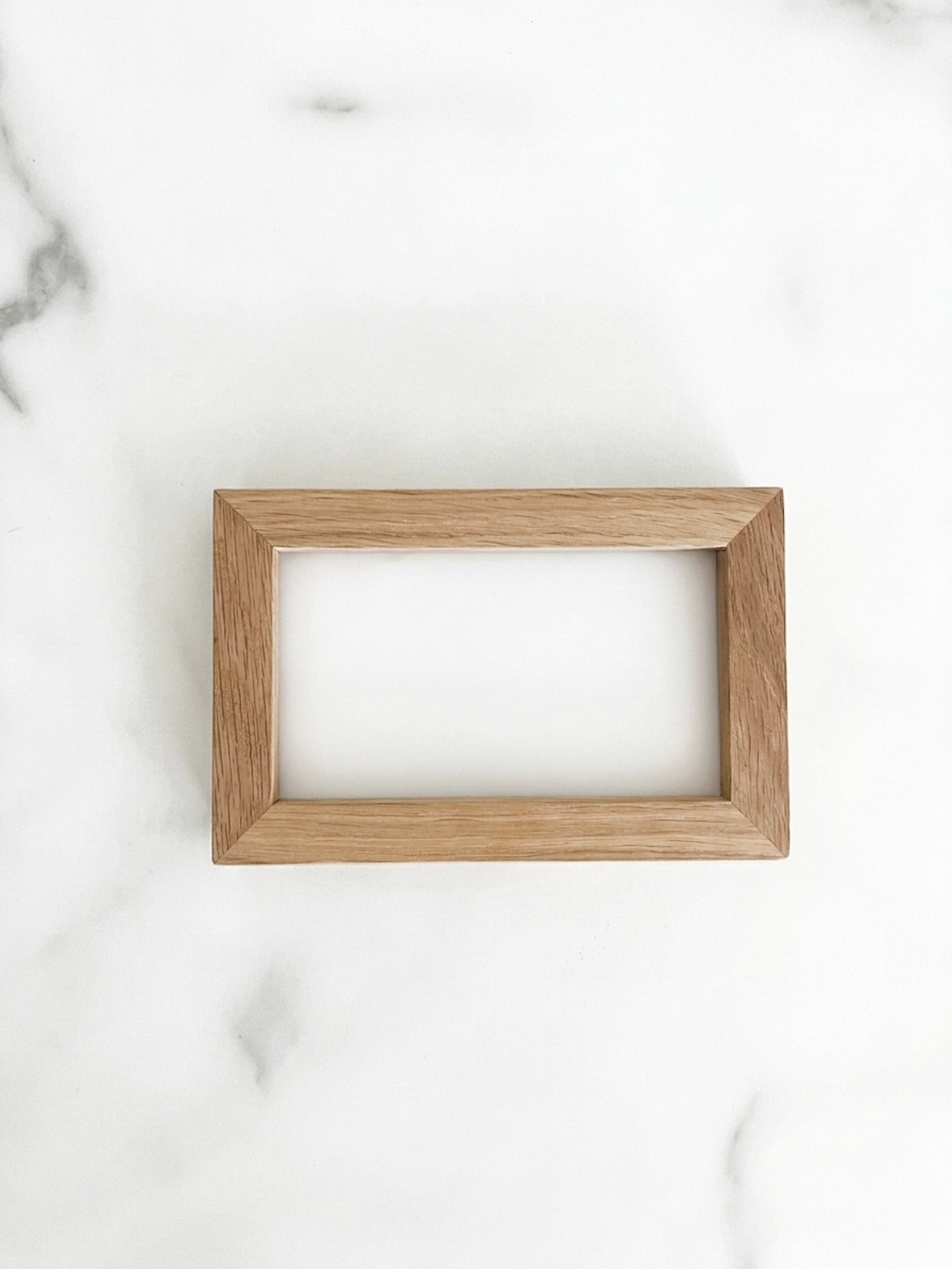 A small 5 inch by 3 inch rectangle natural oak picture frame centered on a light marble background. 