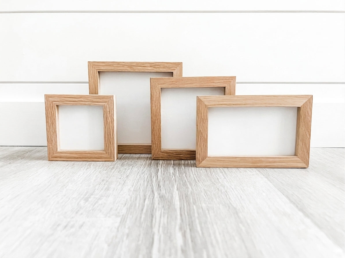 Four empty natural oak wood frames in 5x5, 4x4, 3x3, and 5x3 inch sizes arranged on a white background and gray surface.
