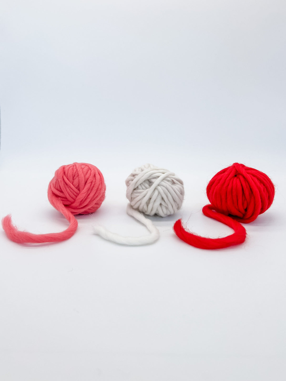 Picture of three yarn balls coral, white and red