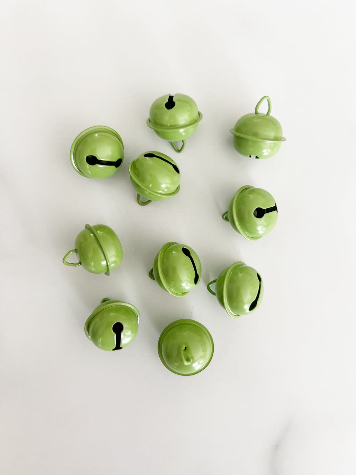 Ten small light green jingle bells arranged on a plain white background.