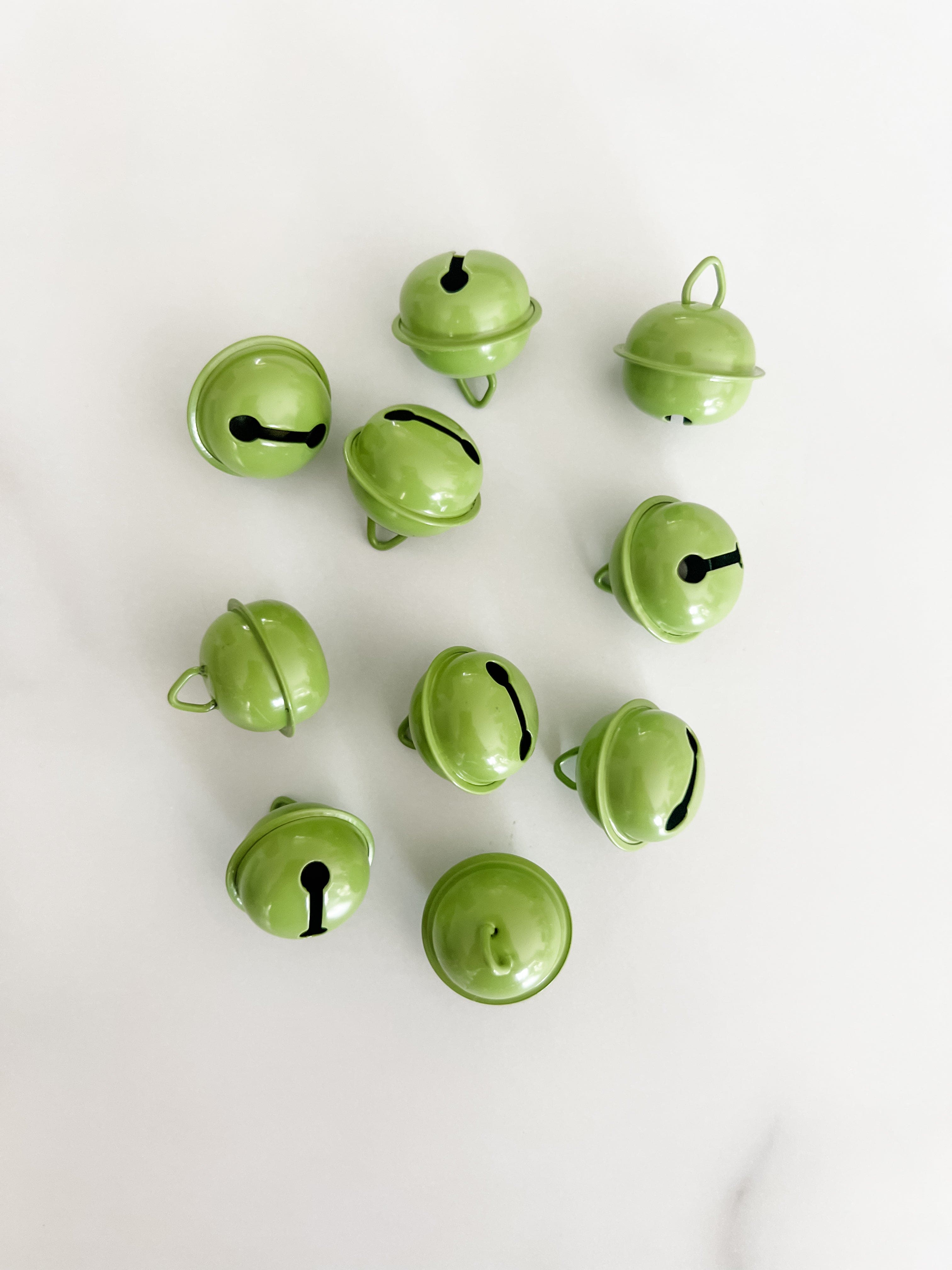 Ten small light green jingle bells arranged on a plain white background.