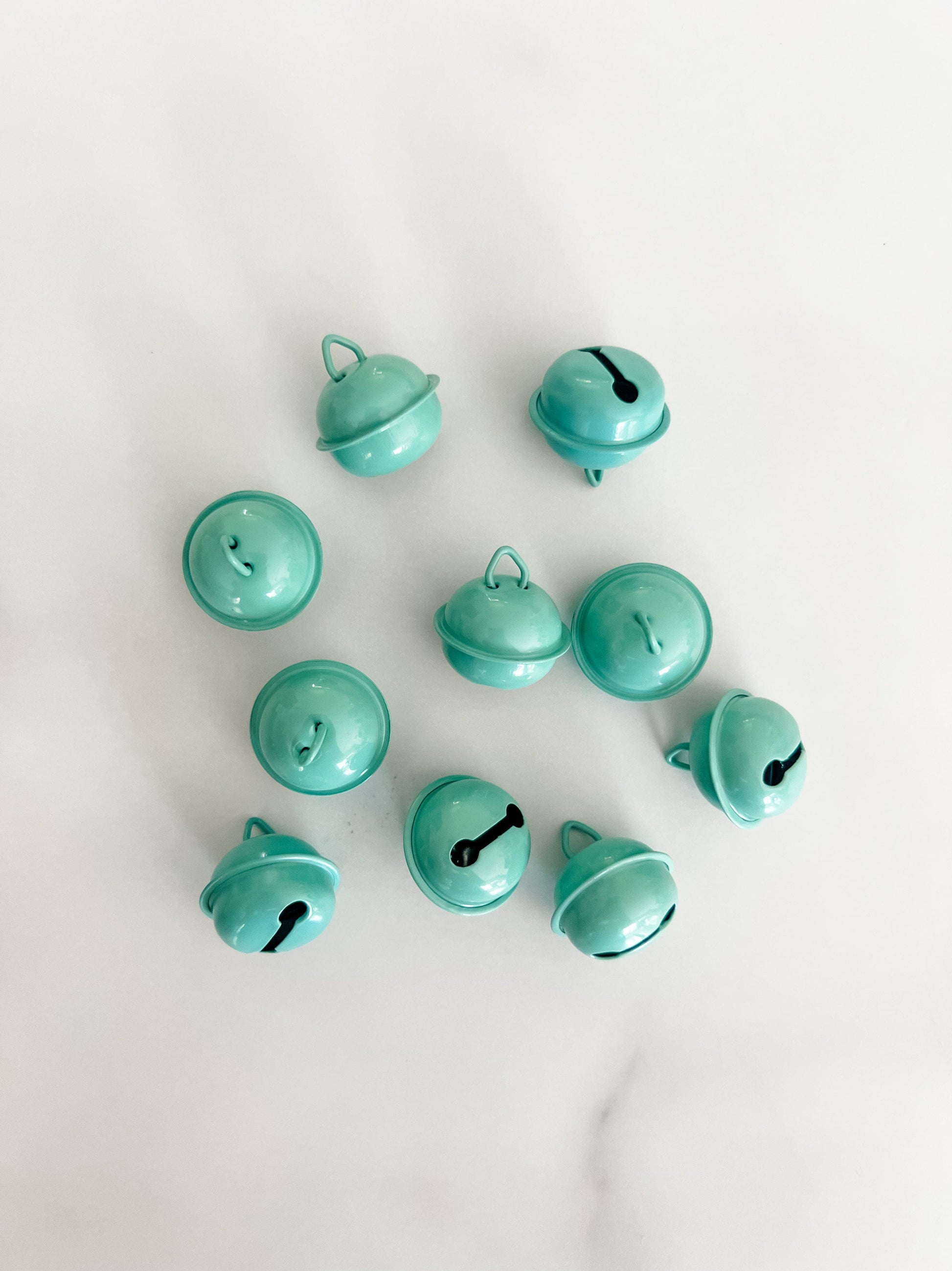 Ten small glossy mint green jingle bells arranged in a loose circle on a light white marble surface.