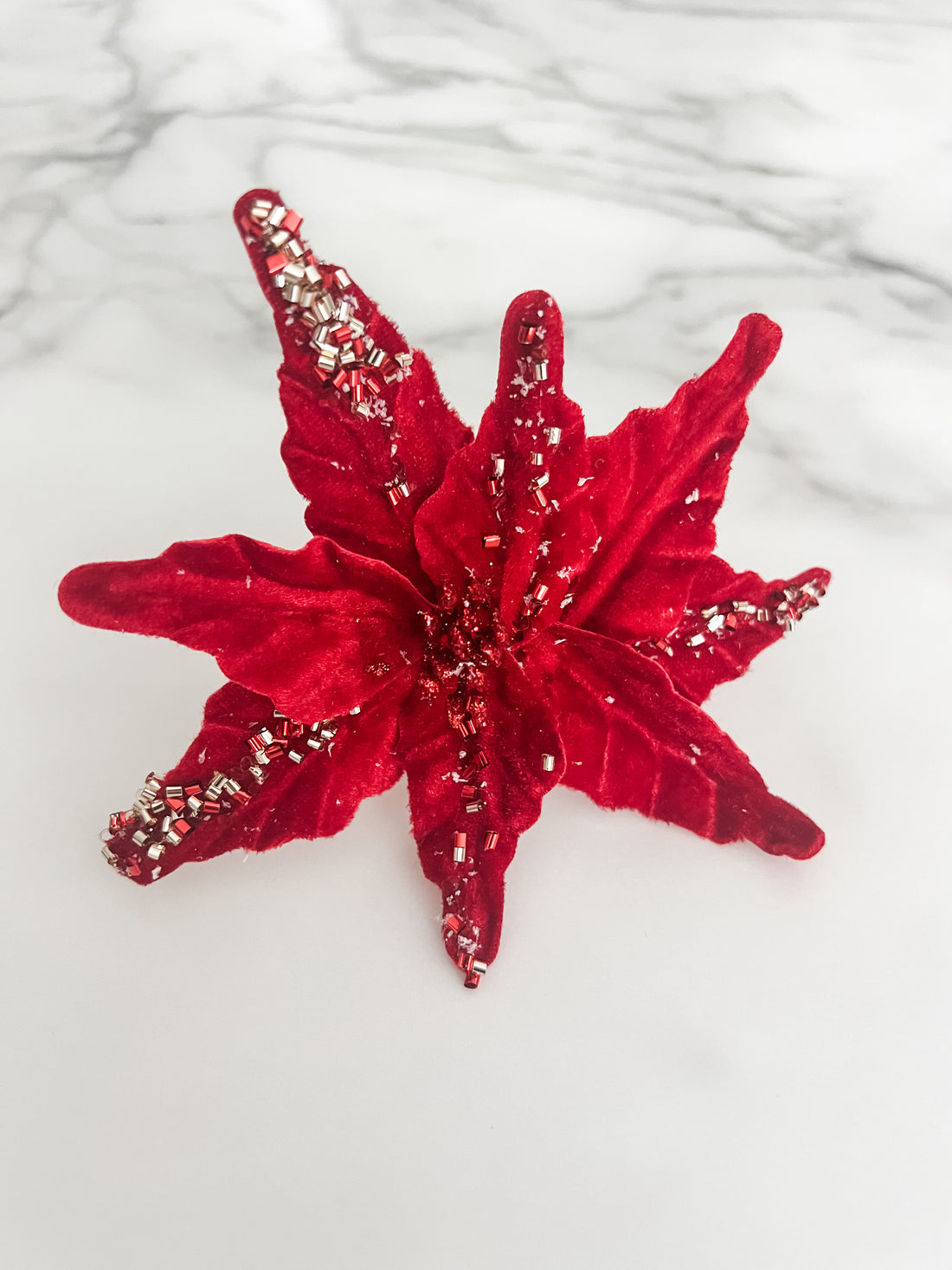 A red beaded poinsettia flower accessory displayed on a white marble surface.