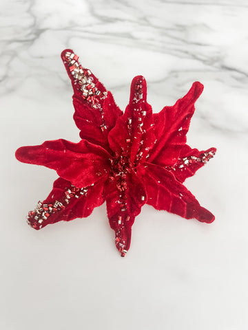 A red beaded poinsettia flower accessory displayed on a white marble surface.