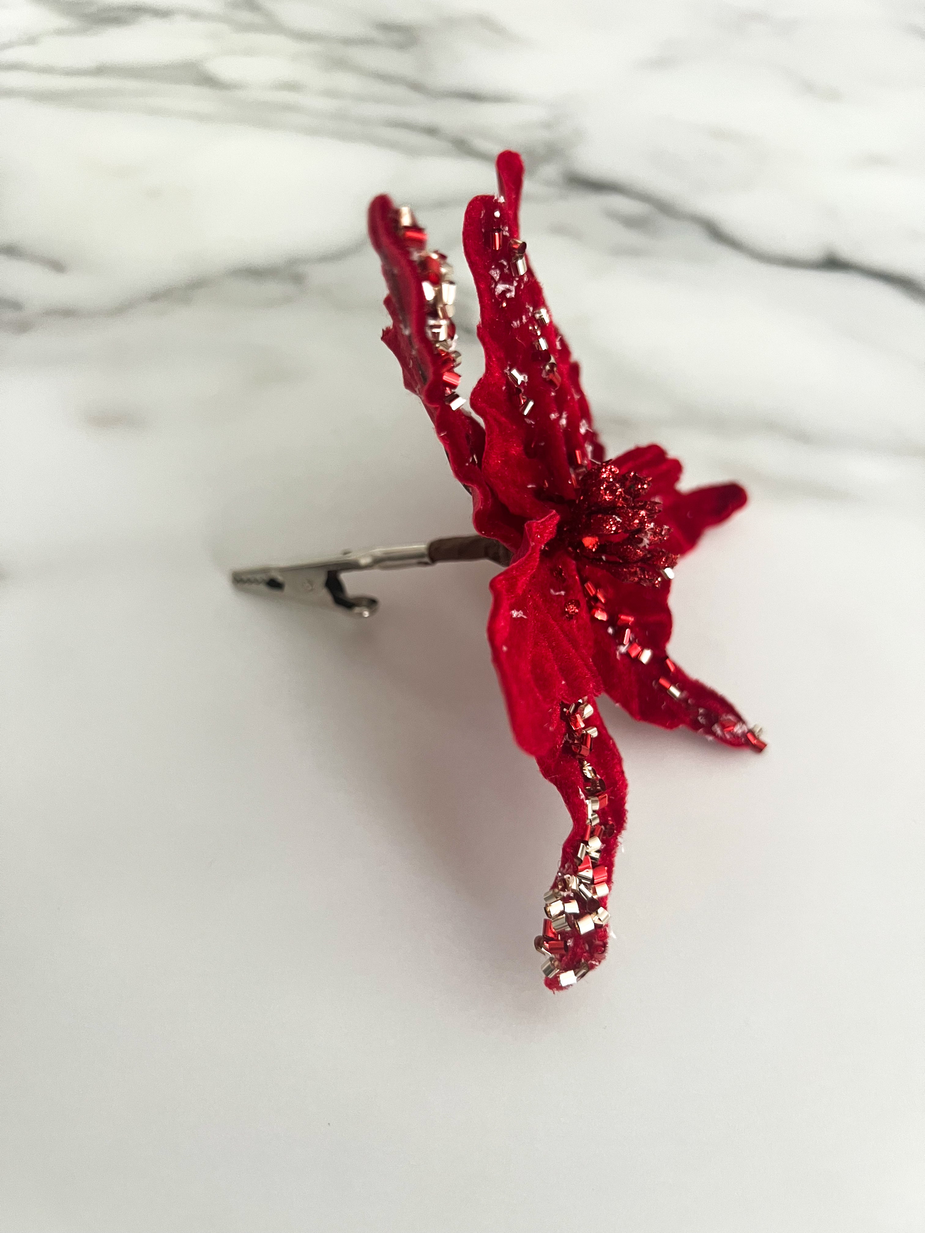 A red beaded poinsettia flower accessory displayed on a white marble surface with a silver clip.
