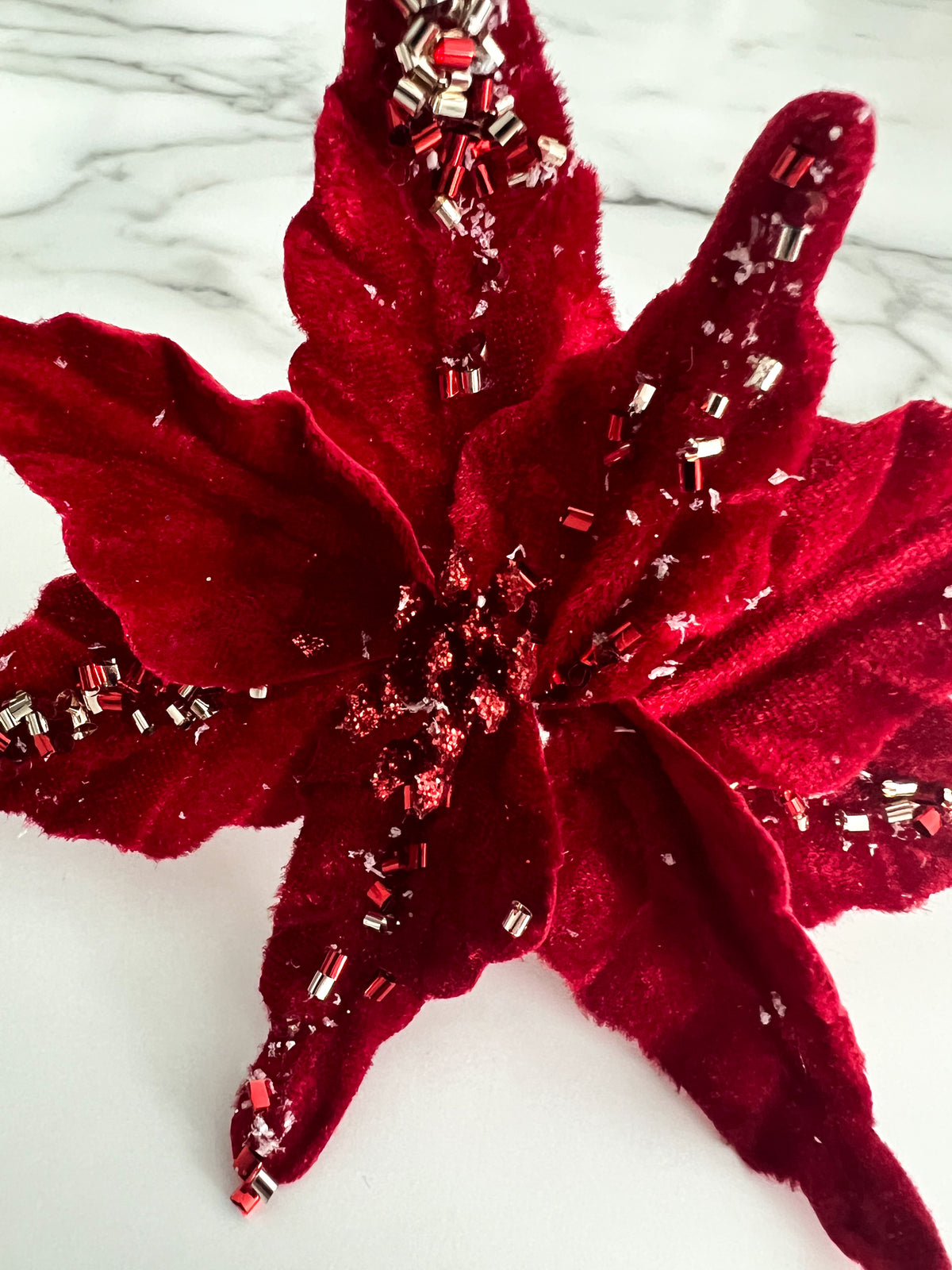 A red beaded poinsettia flower accessory displayed on a white marble surface.