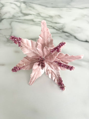 A pink beaded poinsettia flower accessory displayed on a white marble surface.