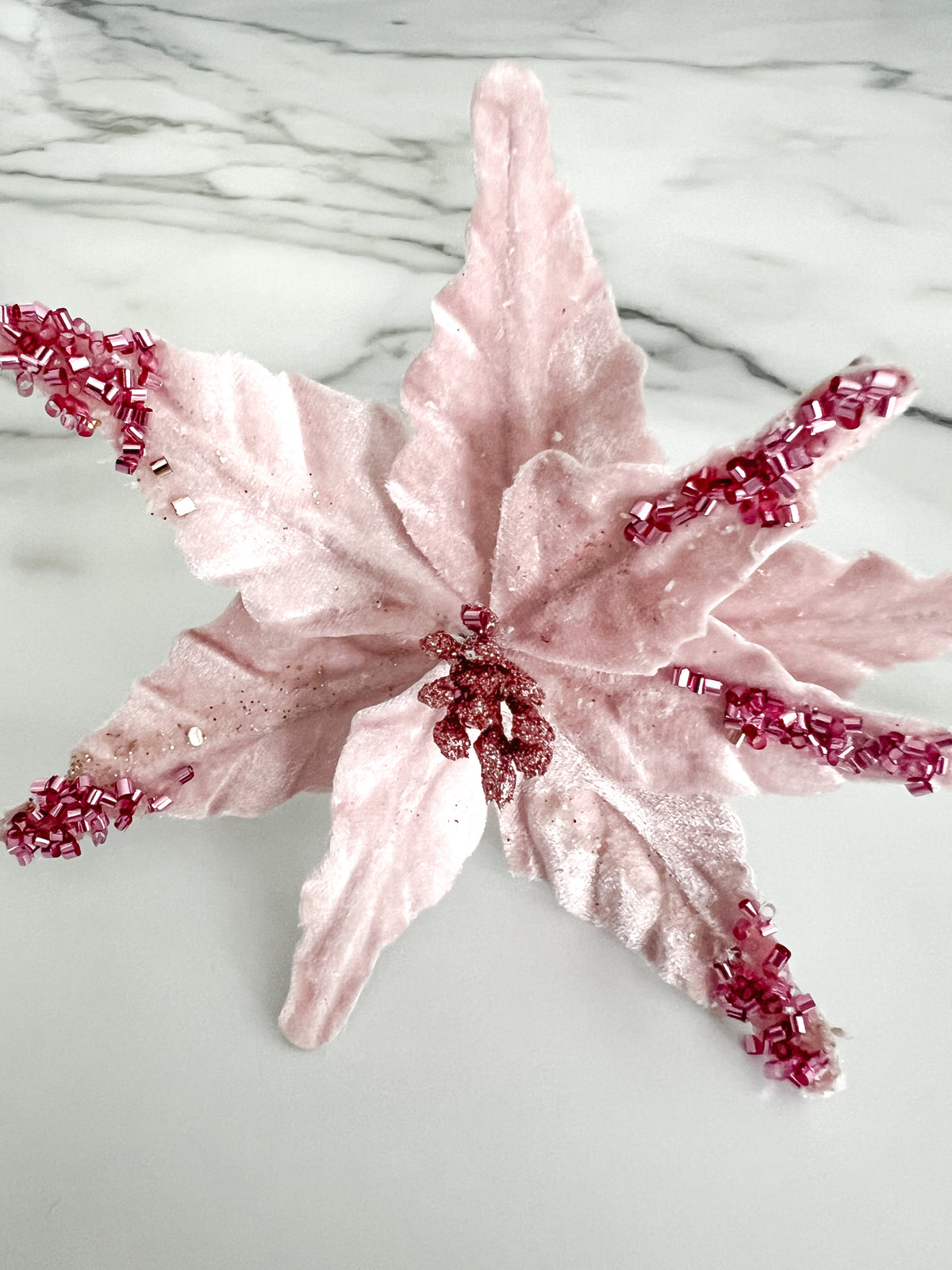 A pink beaded poinsettia flower accessory displayed on a white marble surface.