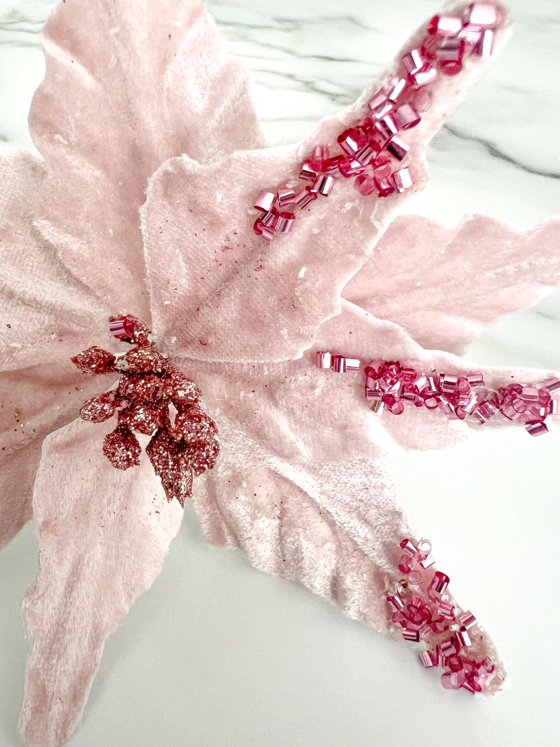 Close up of a pink beaded poinsettia flower accessory displayed on a white marble surface.