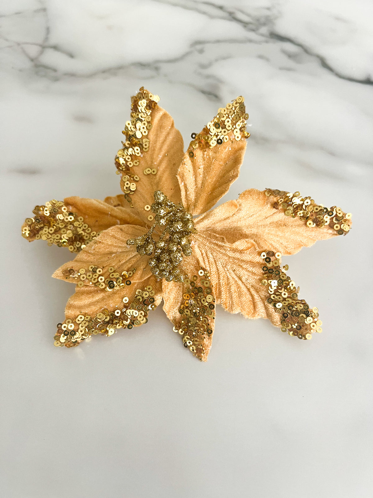 A gold sequined poinsettia flower accessory displayed on a white marble surface.