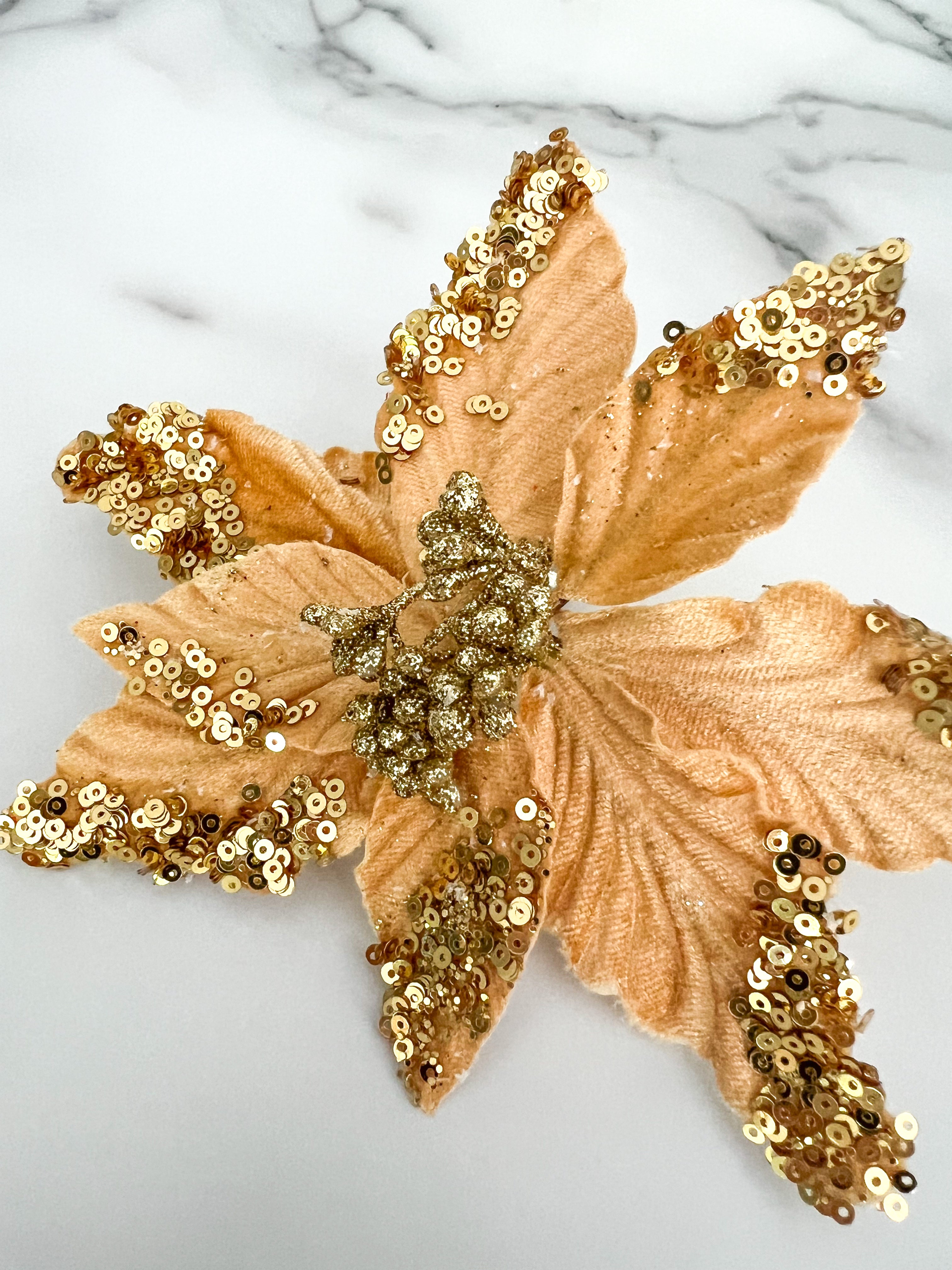 A gold sequined poinsettia flower accessory displayed on a white marble surface.