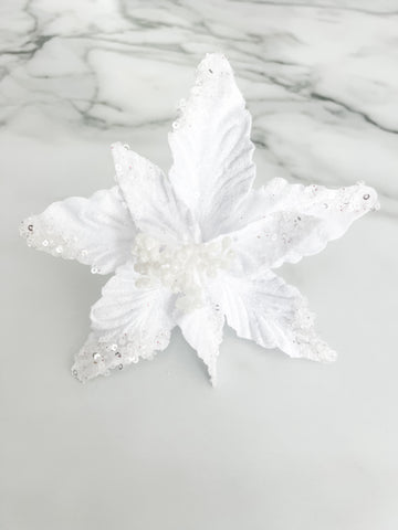 A white faux floral ornament or decorative topper with textured, glittery petals and small bead details, displayed on a light gray marble-patterned surface.