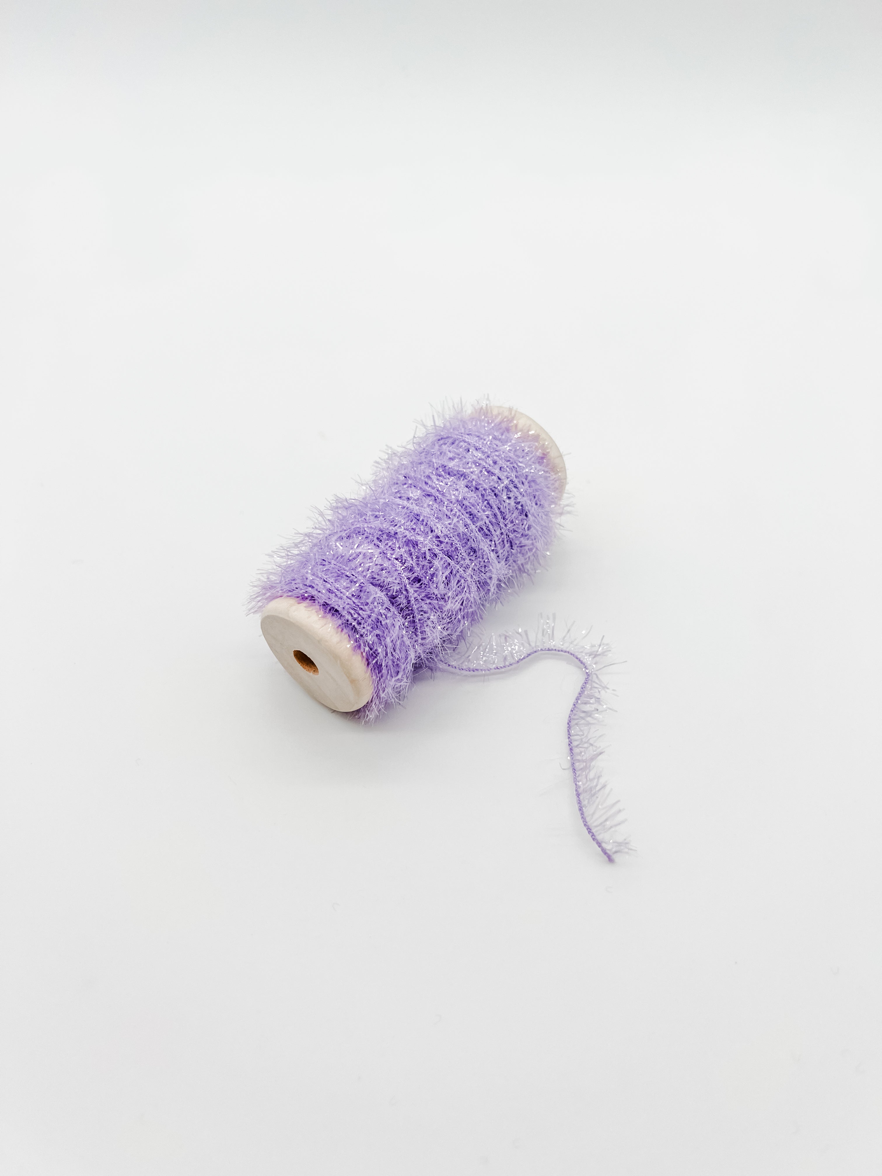 A spool of fluffy, shimmery lavender purple tinsel thread or craft yarn, shown on a plain white background.