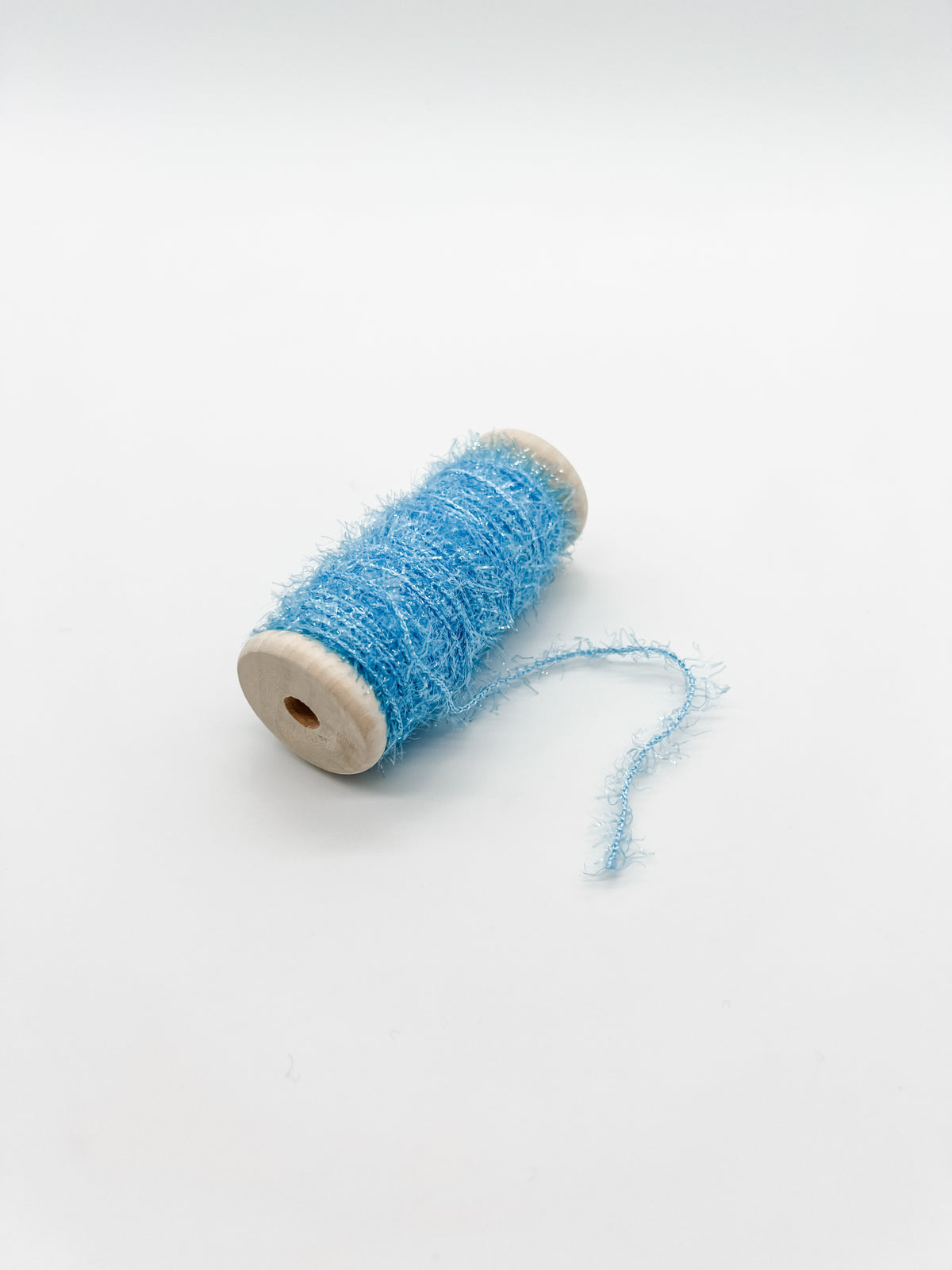 A small spool of fluffy, shimmery light blue thread or yarn resting on a clean white background.