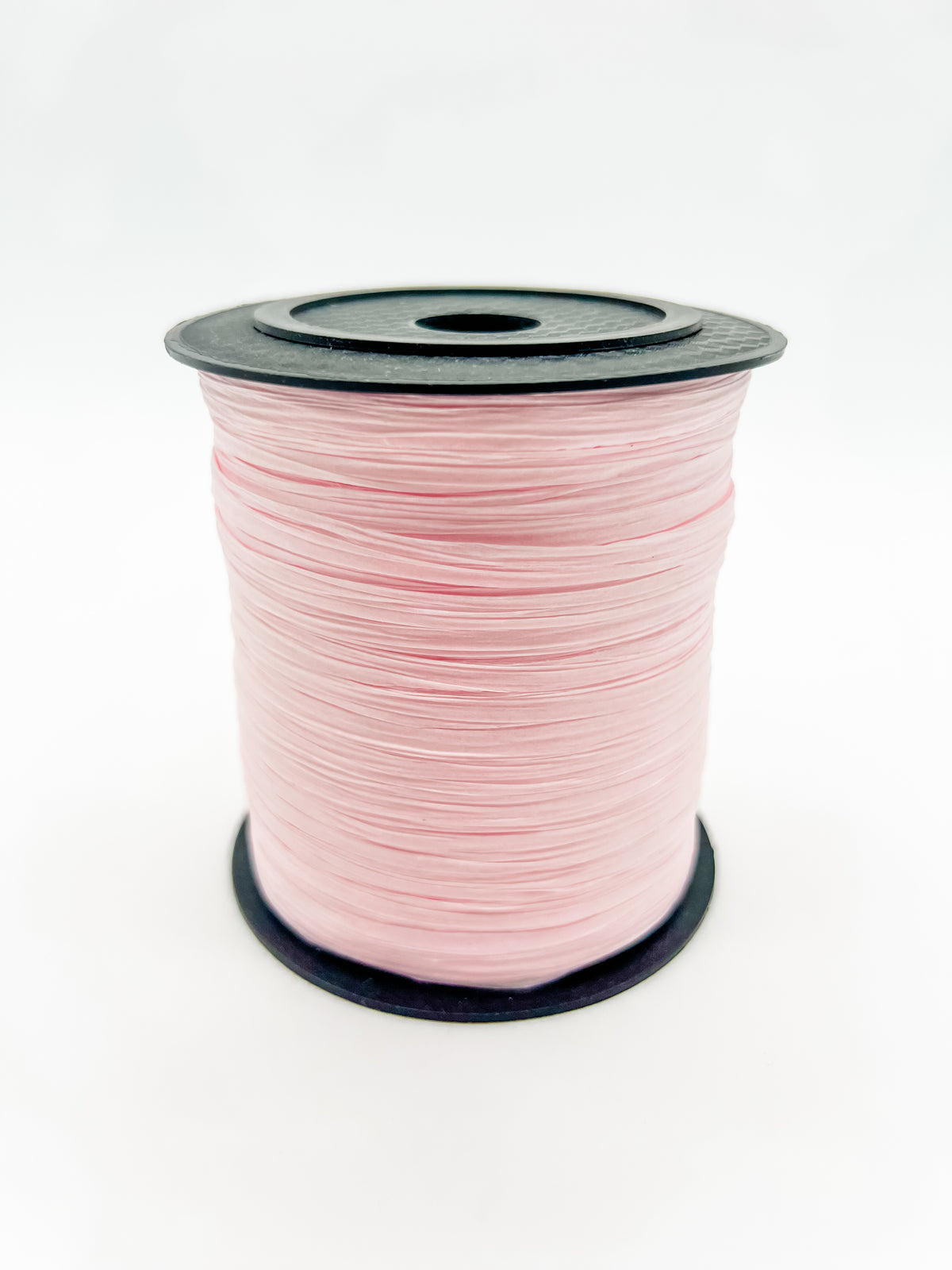 A spool of pale pink paper raffia with a black plastic top and base, photographed on a clean white background.