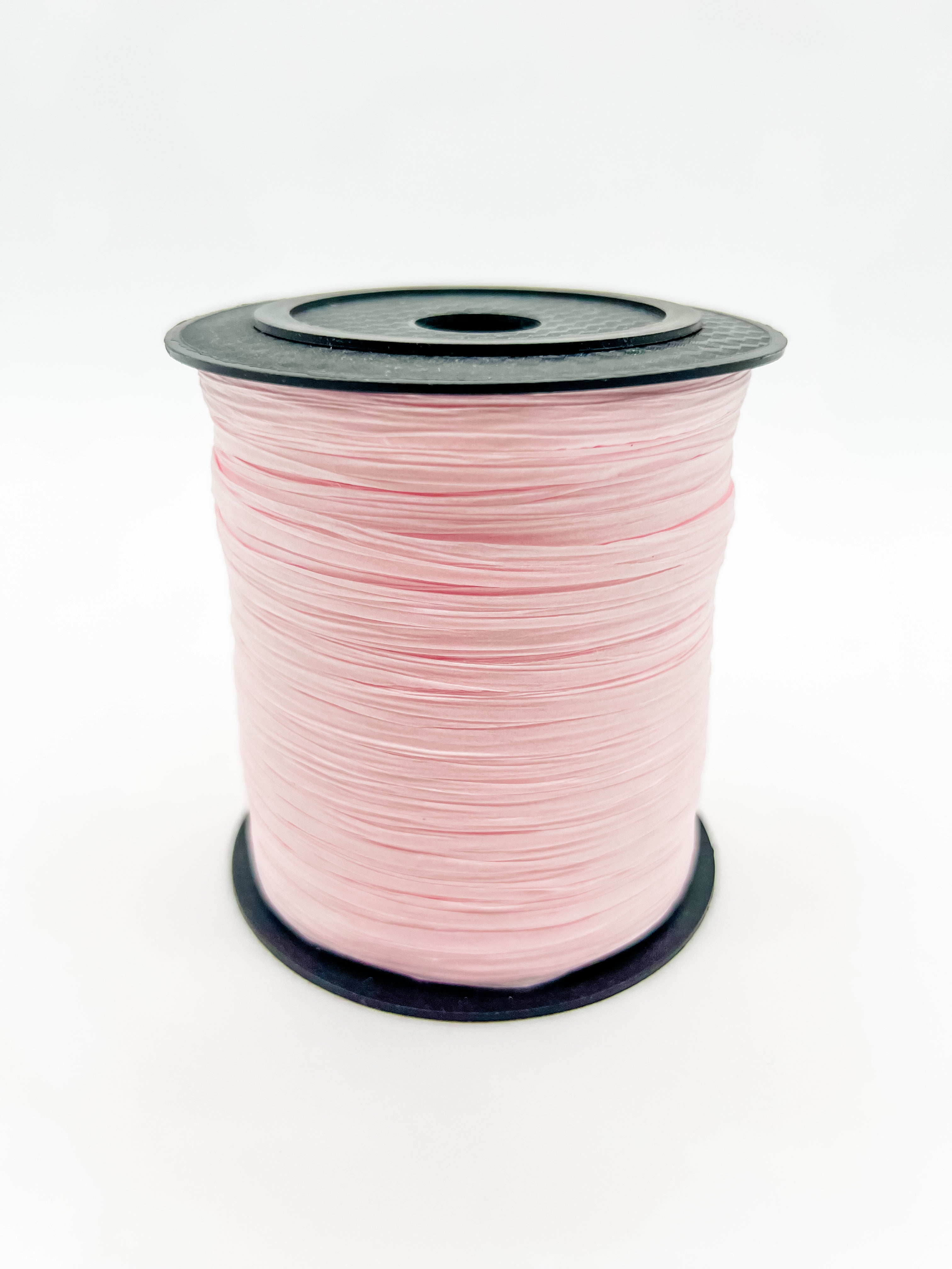 A spool of pale pink paper raffia with a black plastic top and base, photographed on a clean white background.
