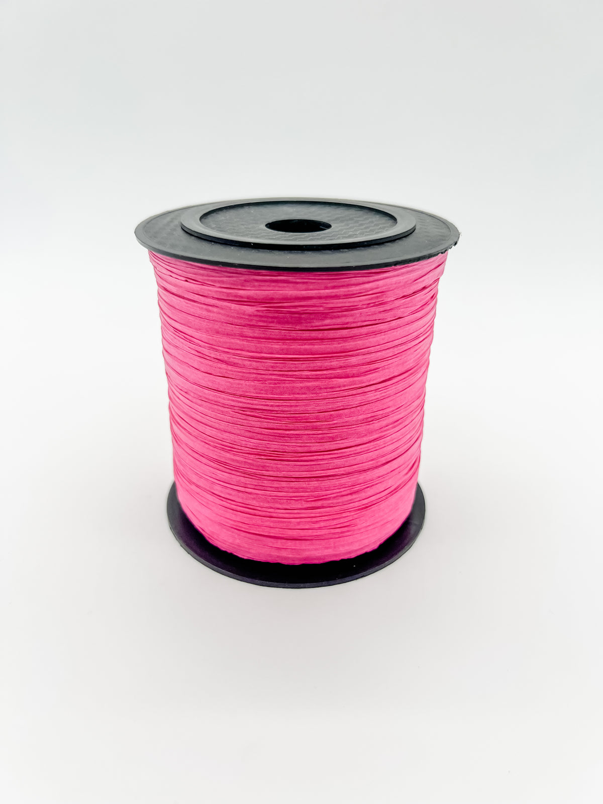 A spool of raspberry pink paper raffia with a black plastic top and base, photographed on a clean white background.