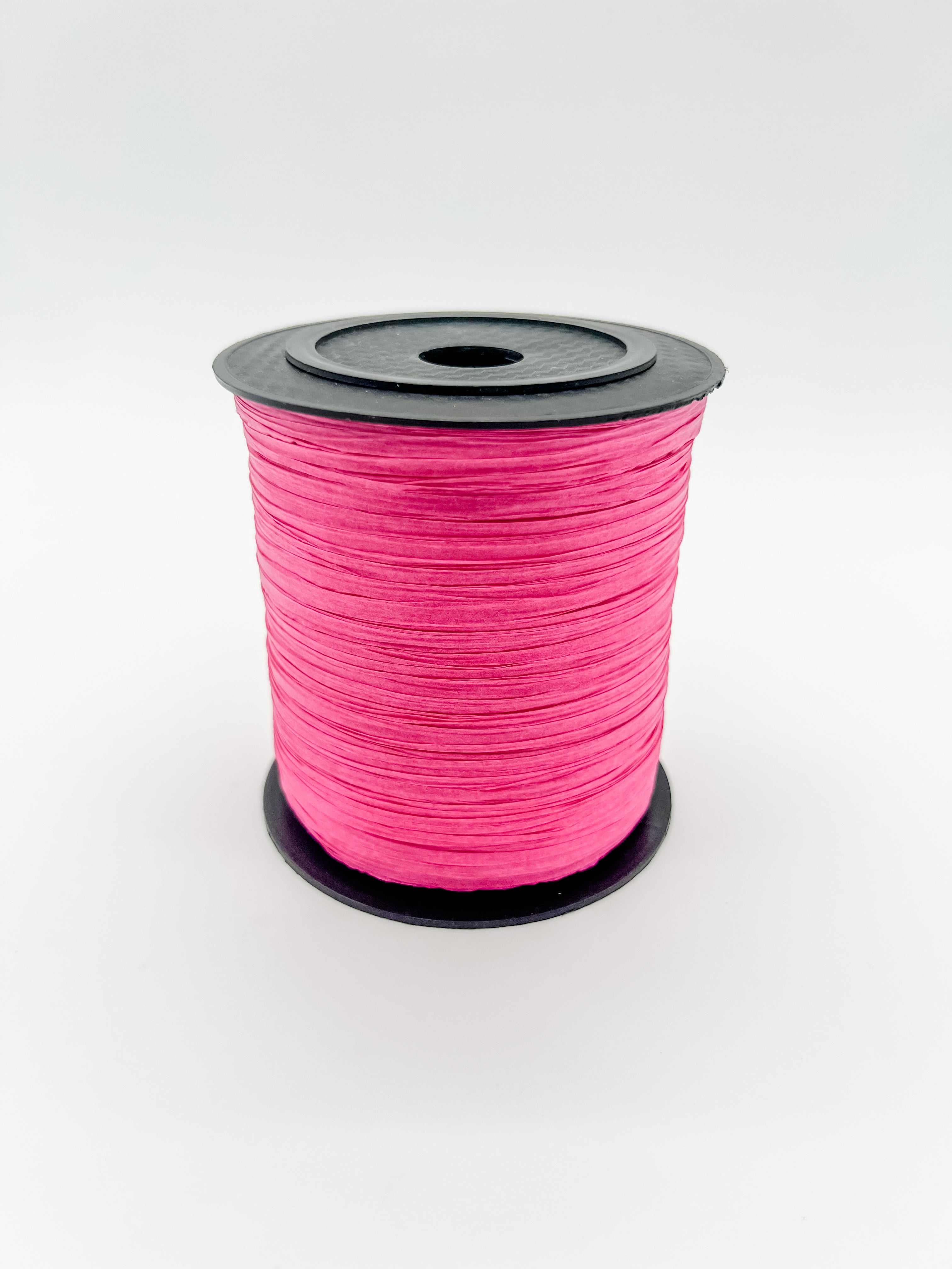 A spool of raspberry pink paper raffia with a black plastic top and base, photographed on a clean white background.