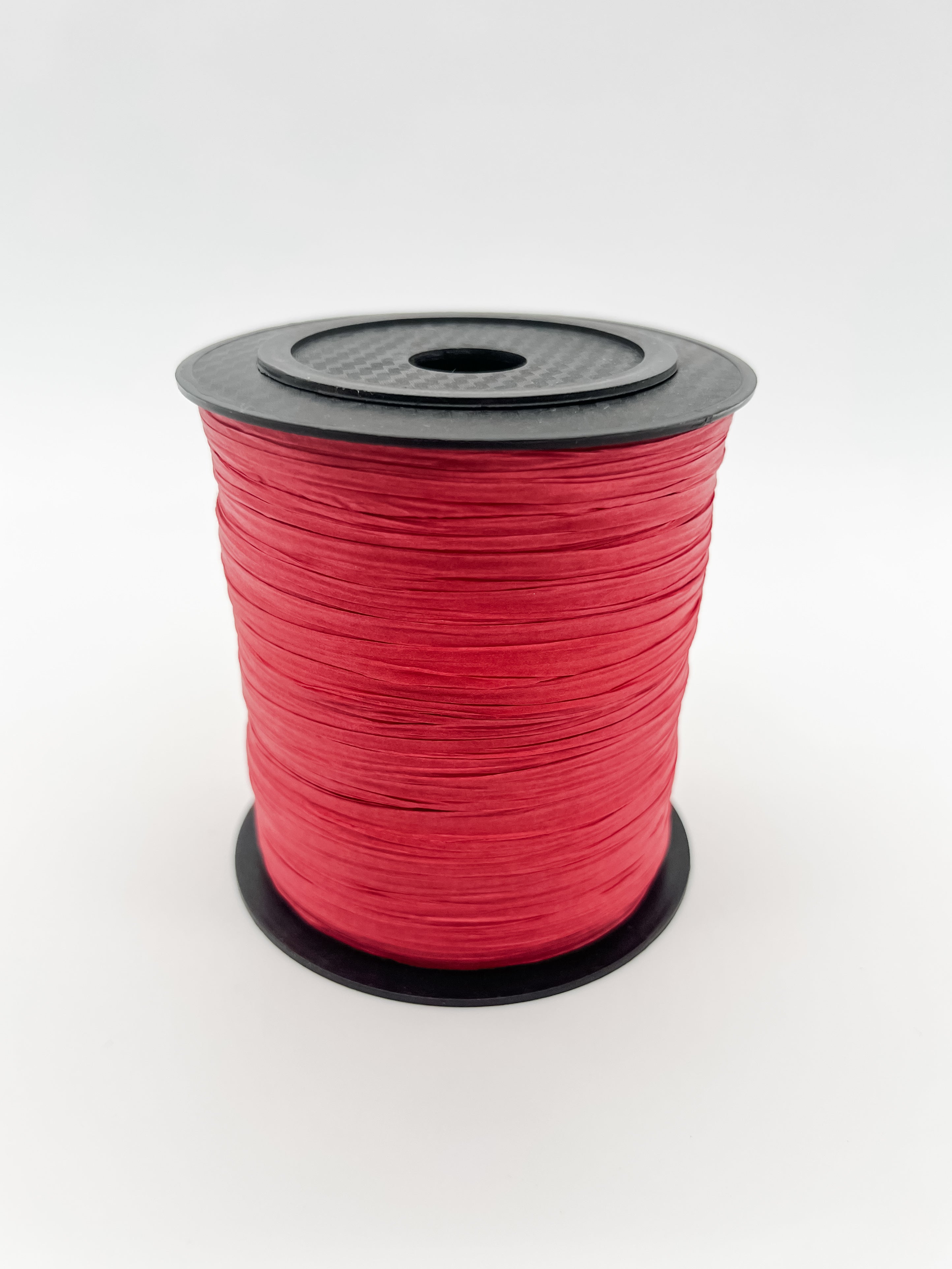 A spool of red paper raffia with a black plastic top and base, photographed on a clean white background.