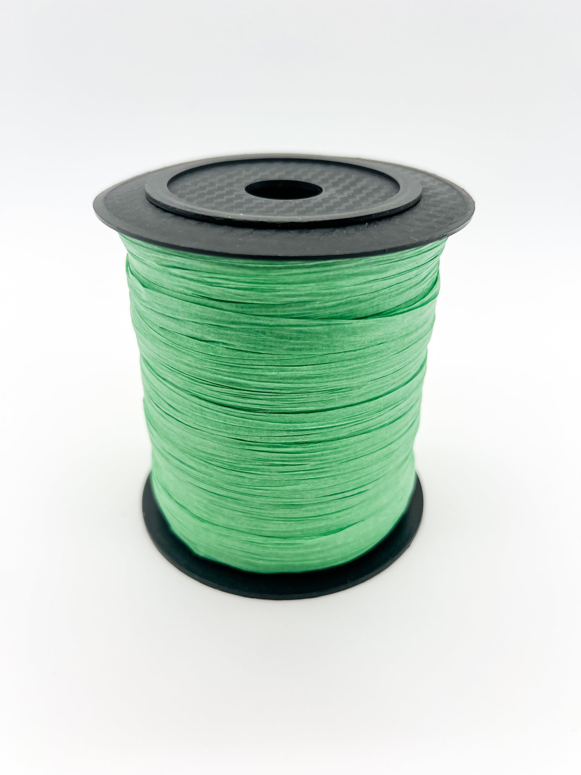 A spool of green paper raffia with a black plastic top and base, photographed on a clean white background.