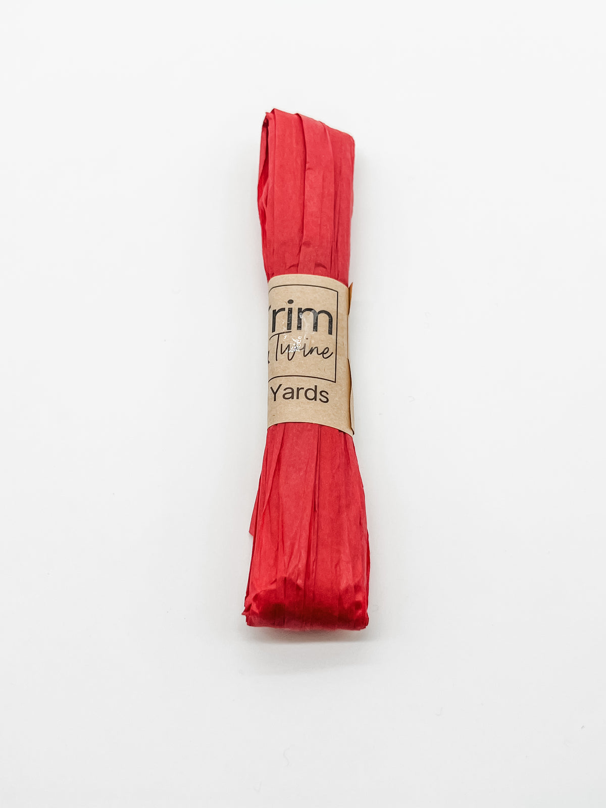 A roll of red raffia wrapped with a brown paper band that reads 'Trim & Twine' and '10 Yards', photographed on a plain white background.