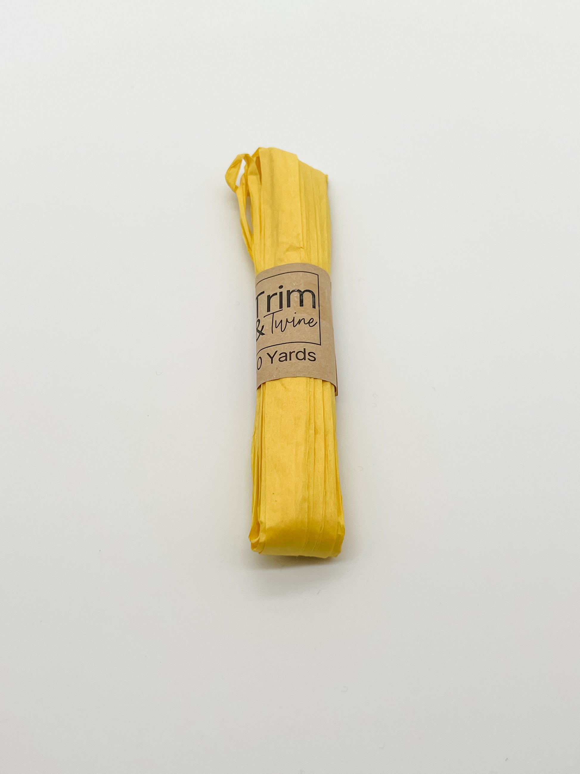 A roll of yellow raffia wrapped with a brown paper band that reads 'Trim & Twine' and '10 Yards', photographed on a plain white background.