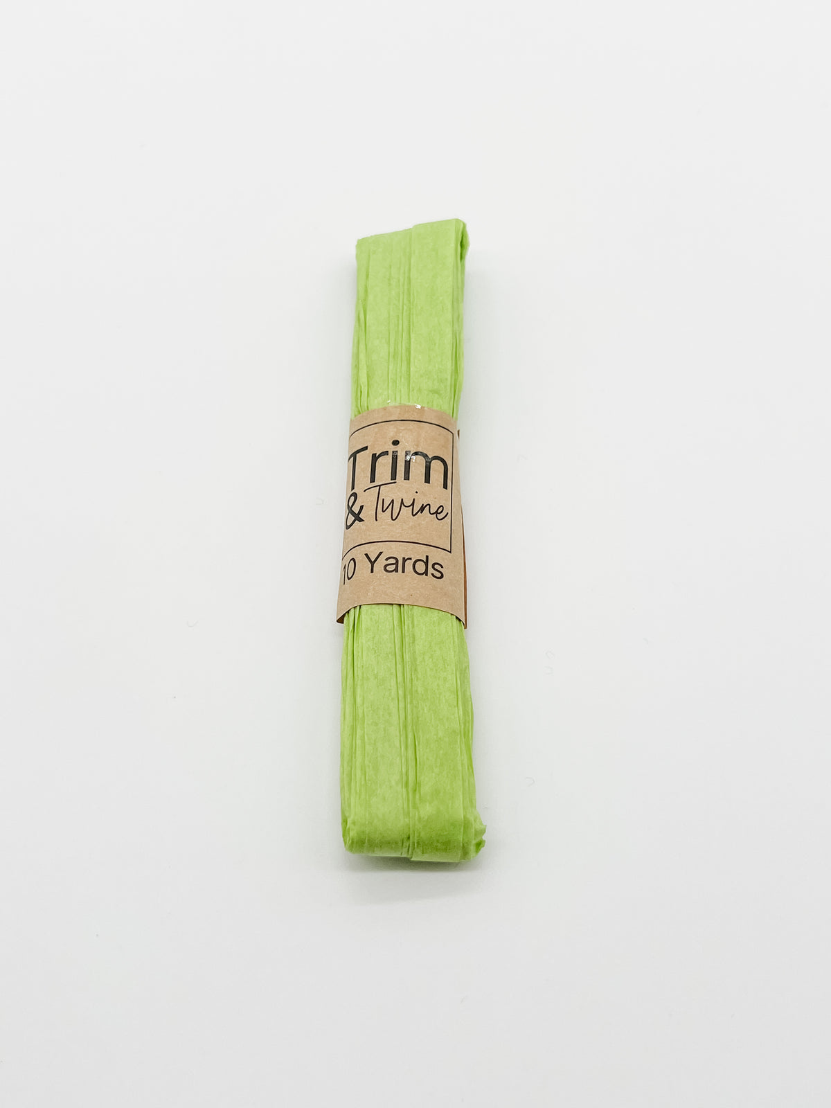 A roll of lime green raffia wrapped with a brown paper band that reads 'Trim & Twine' and '10 Yards', photographed on a plain white background.