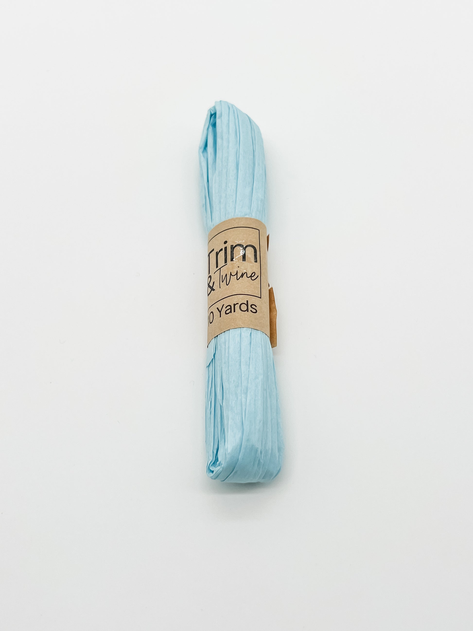 A roll of baby blue raffia wrapped with a brown paper band that reads 'Trim & Twine' and '10 Yards', photographed on a plain white background.