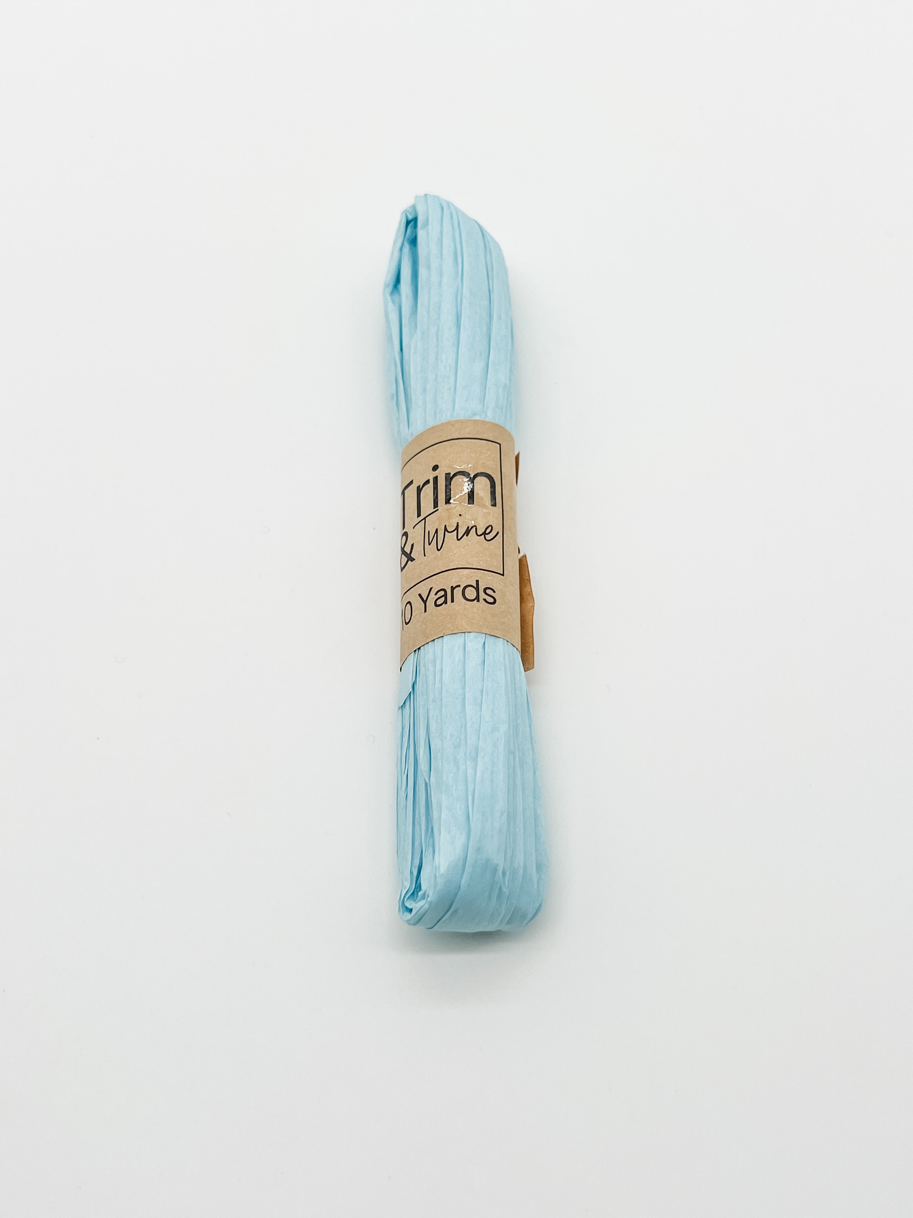 A roll of baby blue raffia wrapped with a brown paper band that reads 'Trim & Twine' and '10 Yards', photographed on a plain white background.