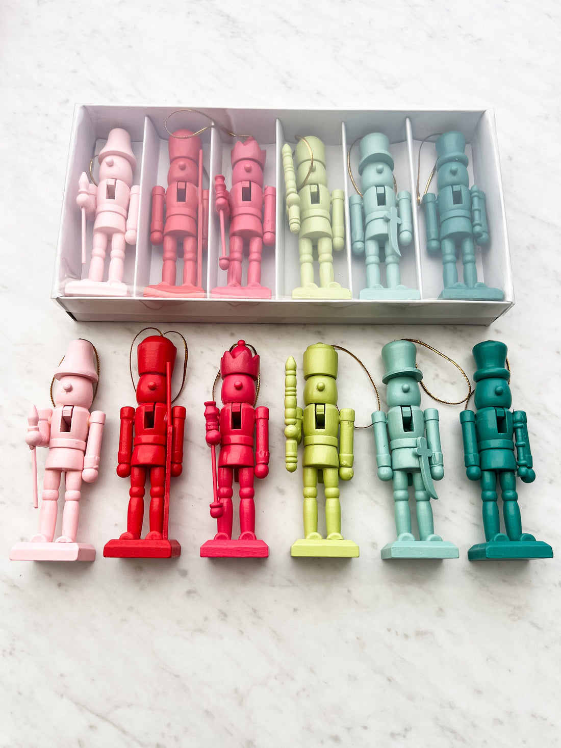 A set of six colorful wooden nutcrackers displayed in a box, with variations in pink, red, green, and blue colors.