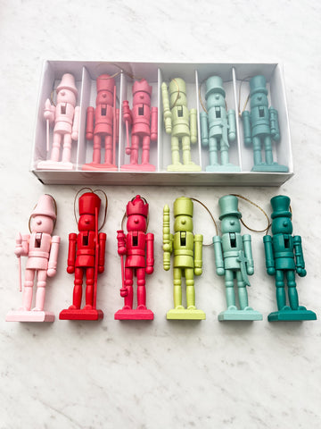 A set of six colorful wooden nutcrackers displayed in a box, with variations in pink, red, green, and blue colors.
