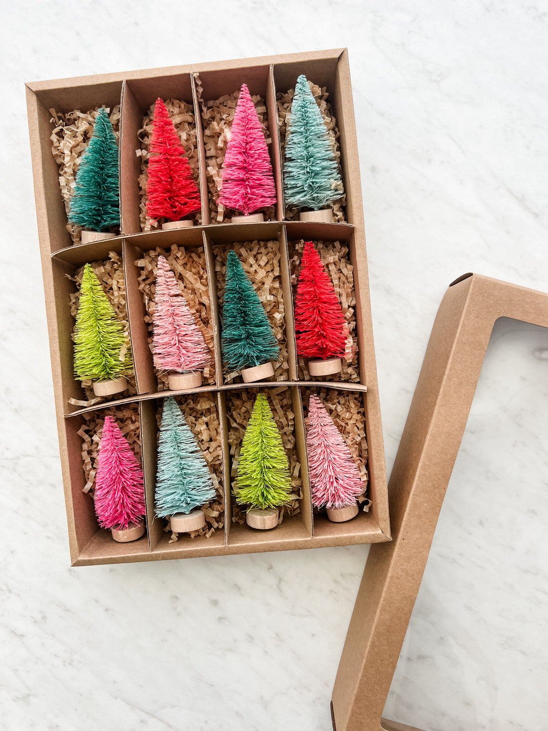 A set of colorful bottle brush trees displayed in an open cardboard box with two trees of each color neatly arranged.
