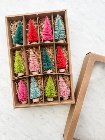 A set of colorful bottle brush trees displayed in an open cardboard box with two trees of each color neatly arranged.