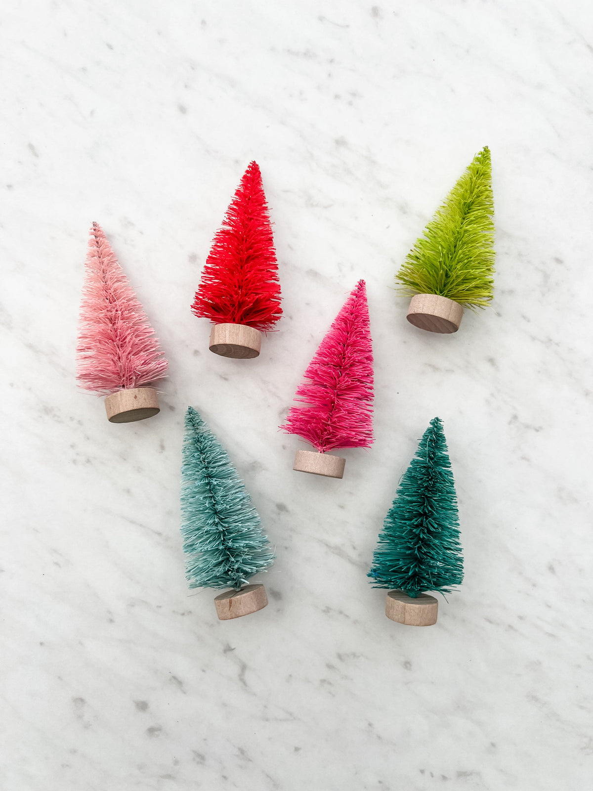 Set of 6 colorful bottle brush christmas trees shown on a white marbled background.