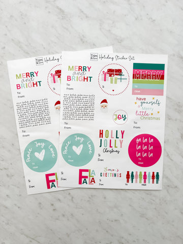 Two sheets of multicolored stickers with holiday greetings laid out on a flat surface.