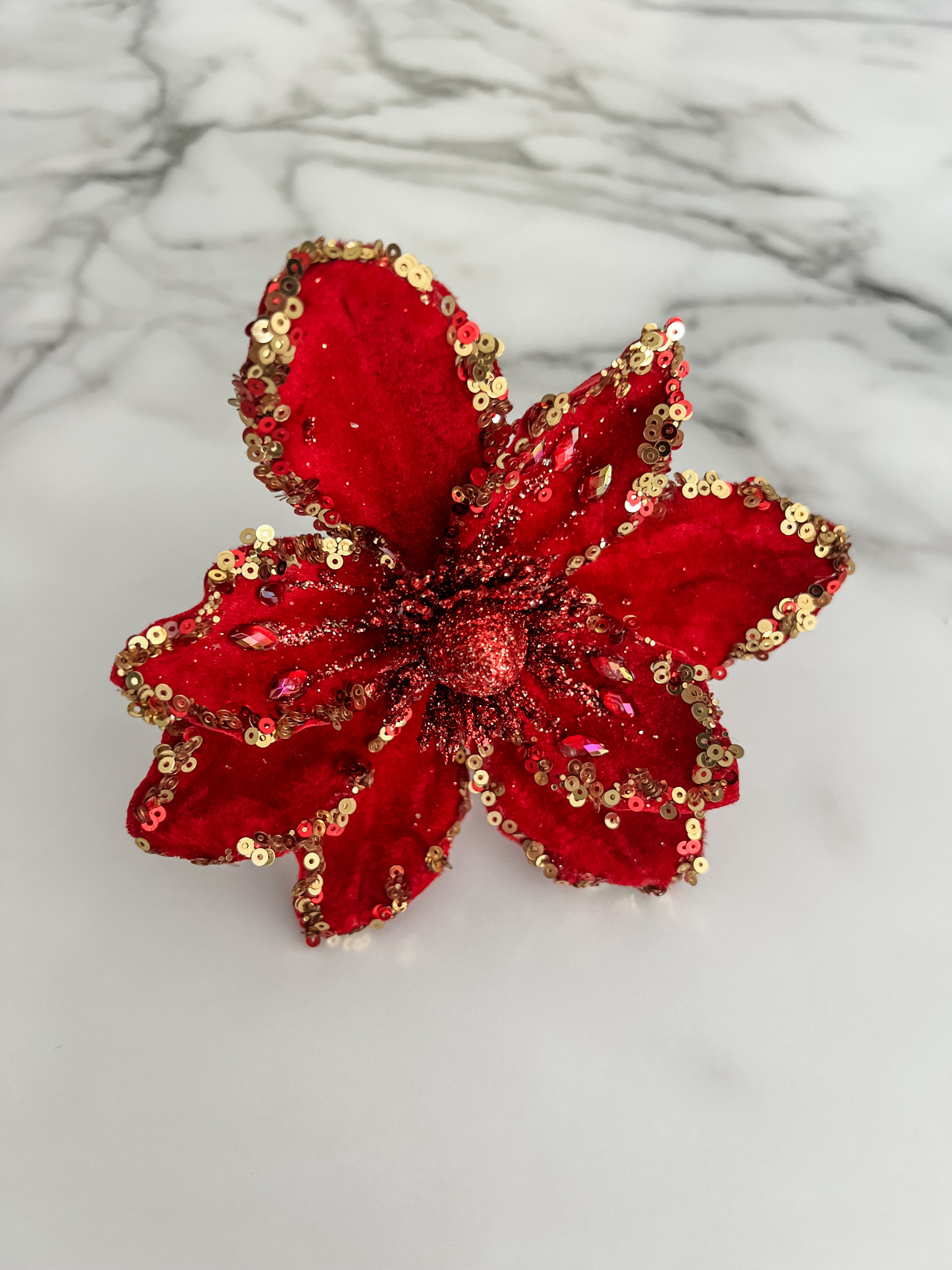 A red sequined poinsettia-style flower embellishment with gold sequined edges, displayed on a white marble surface.
