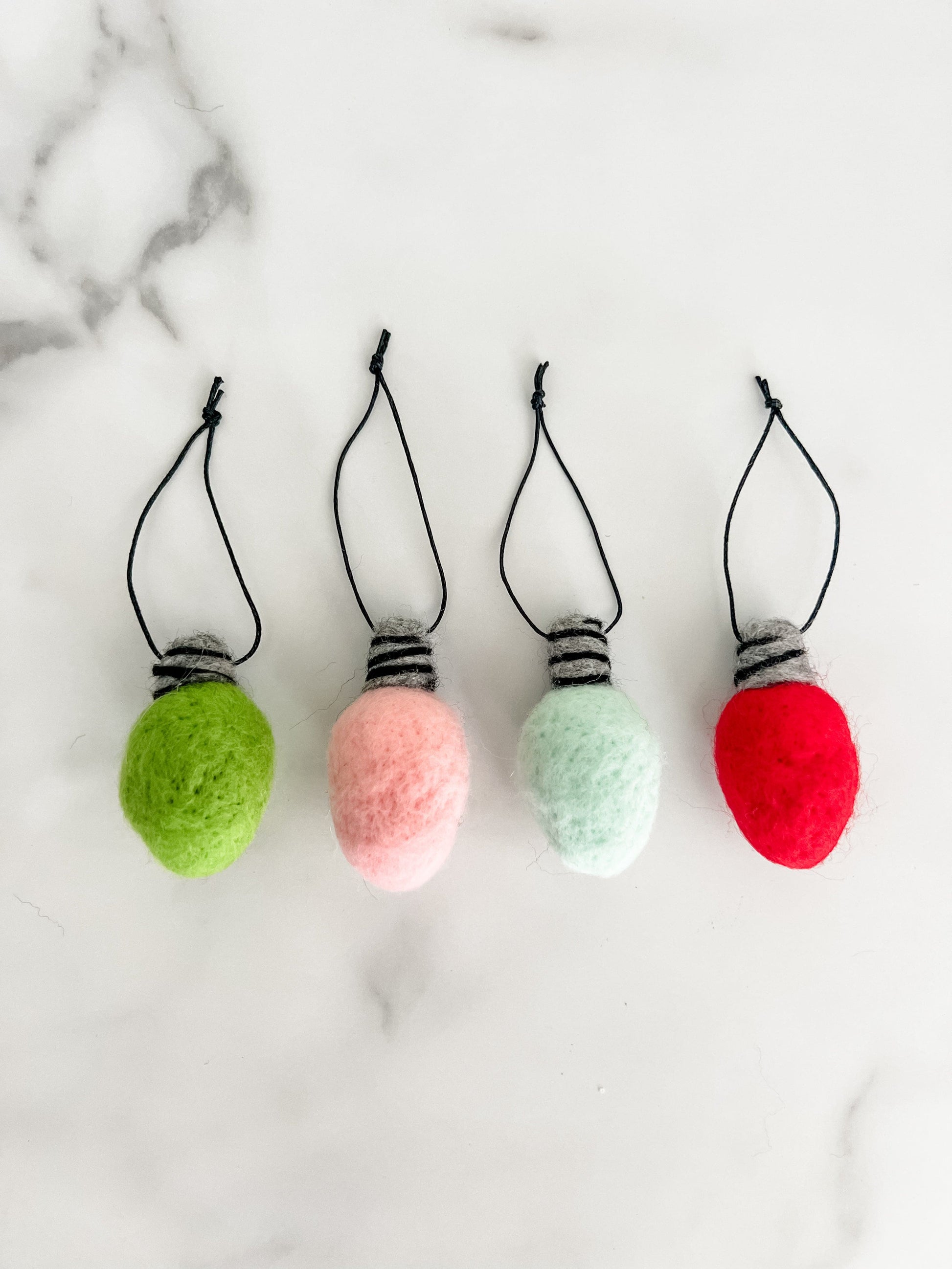 Four colorful felted Christmas bulbs with strings on a marbled background.