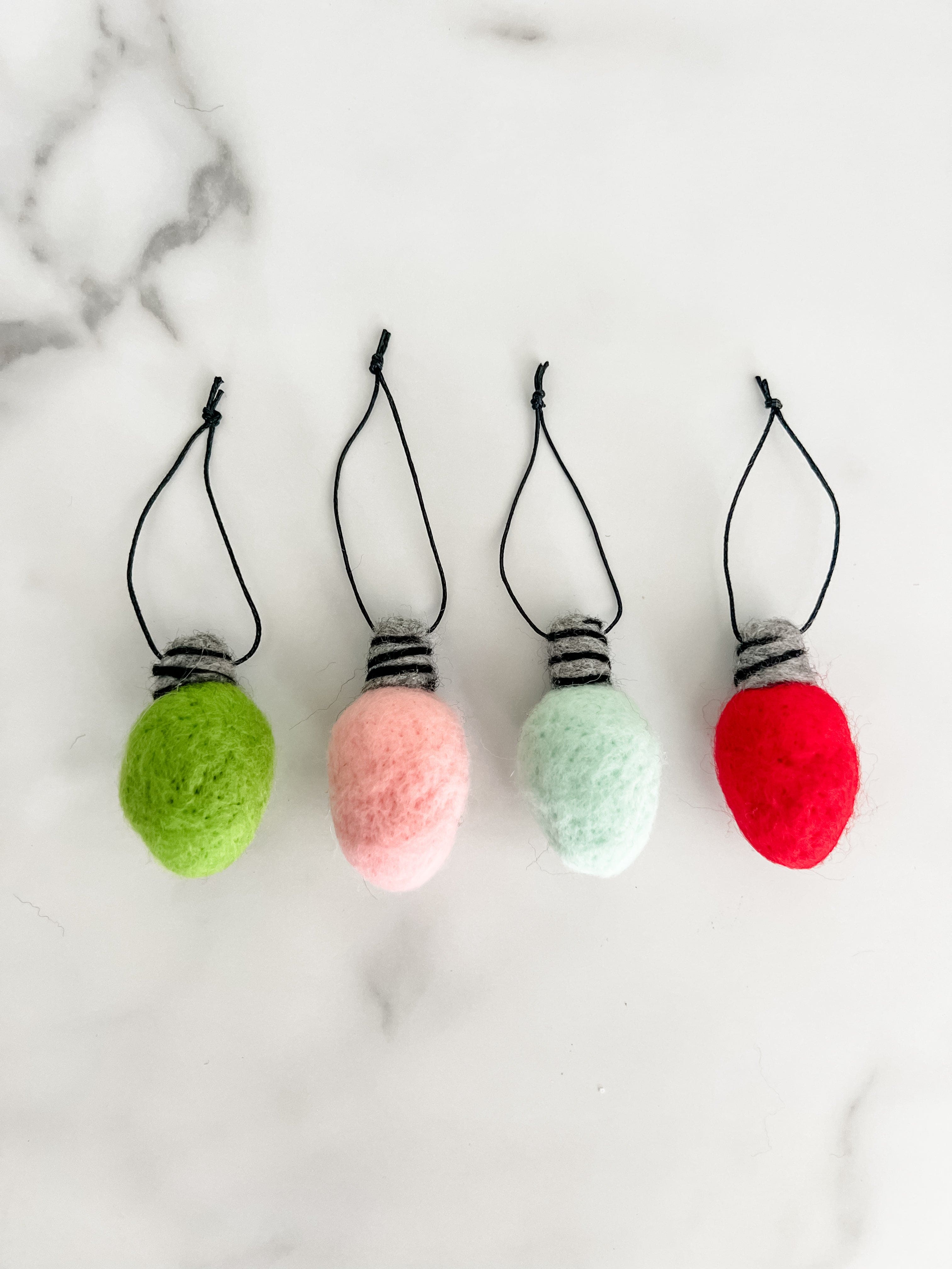 Four colorful felted Christmas bulbs with strings on a marbled background.