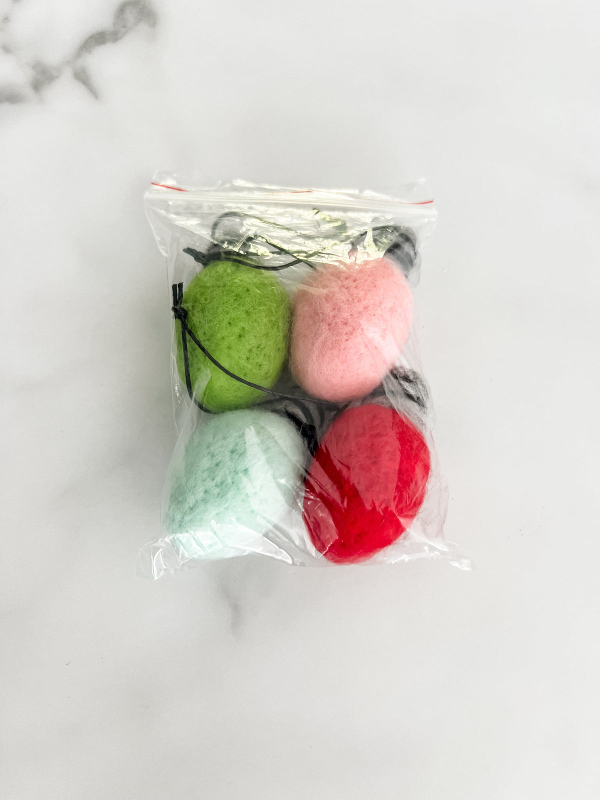 Four colorful Christmas bulbs packaged in a clear bag on a white marbled surface.