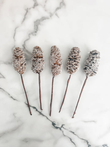 Five decorative pinecone sticks with a textured finish on a marble surface