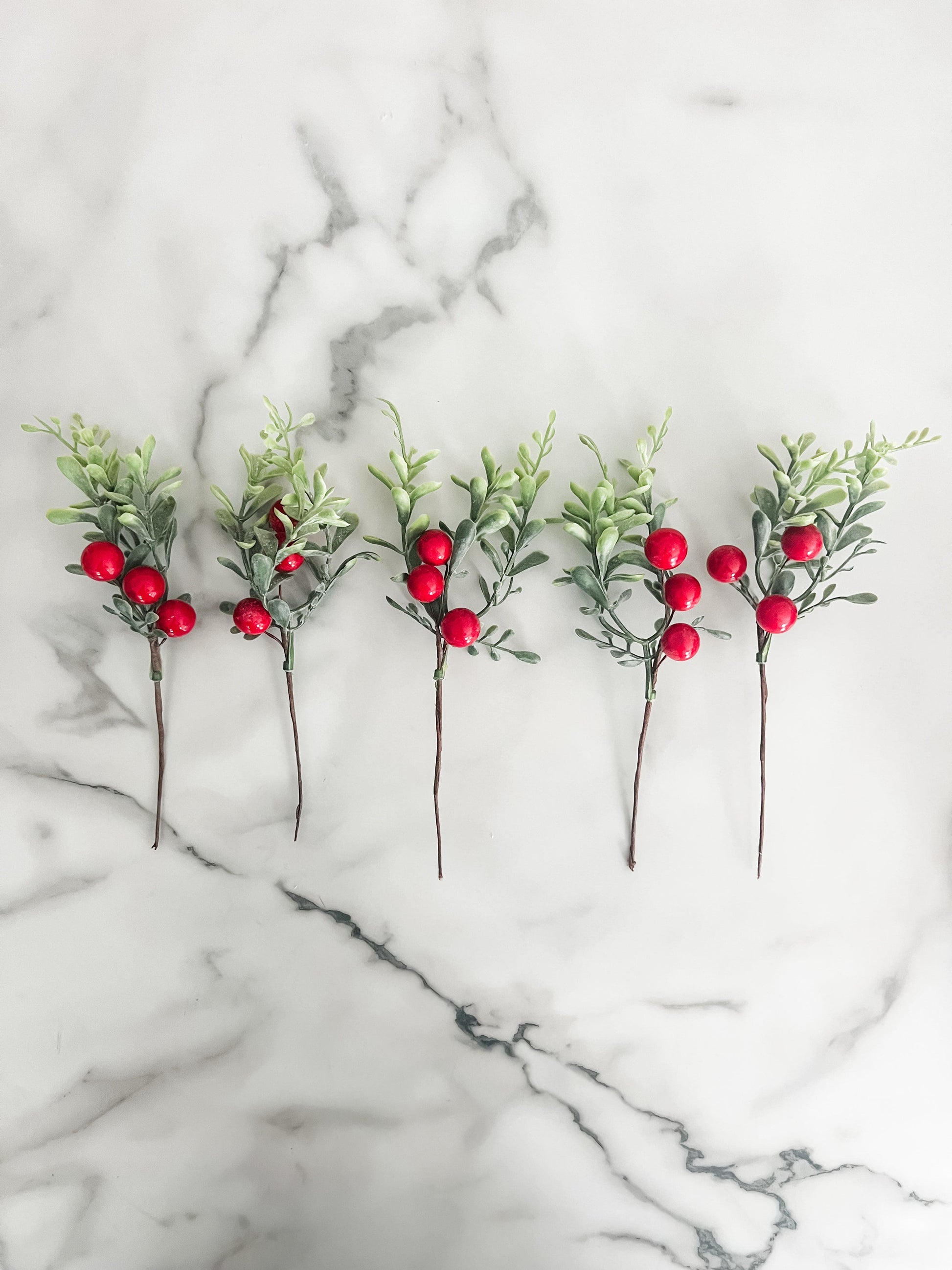 Five artificial greenery sticks with red berries on a marble surface