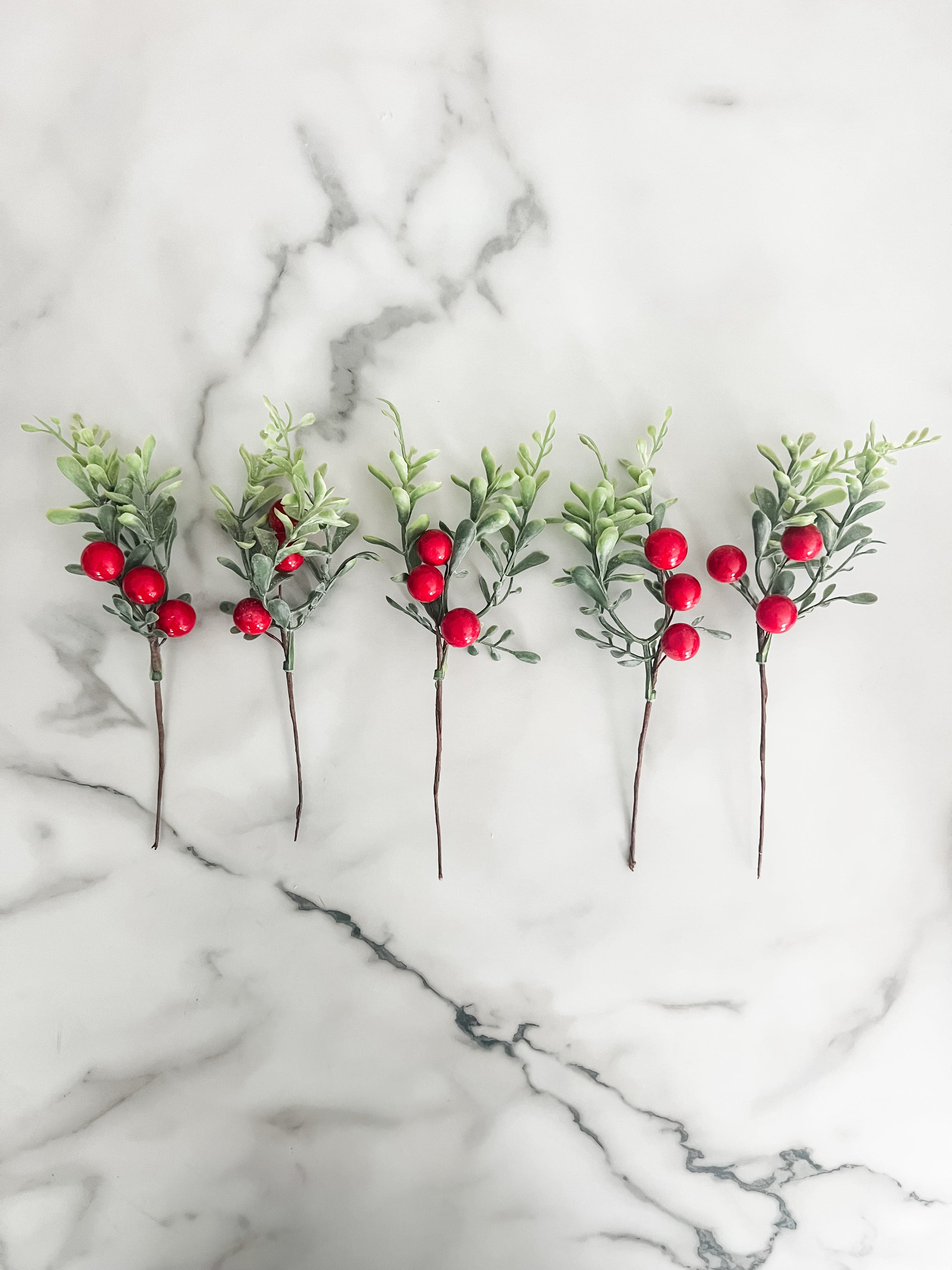 Five artificial greenery sticks with red berries on a marble surface