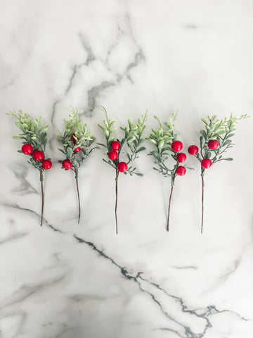 Five artificial greenery sticks with red berries on a marble surface