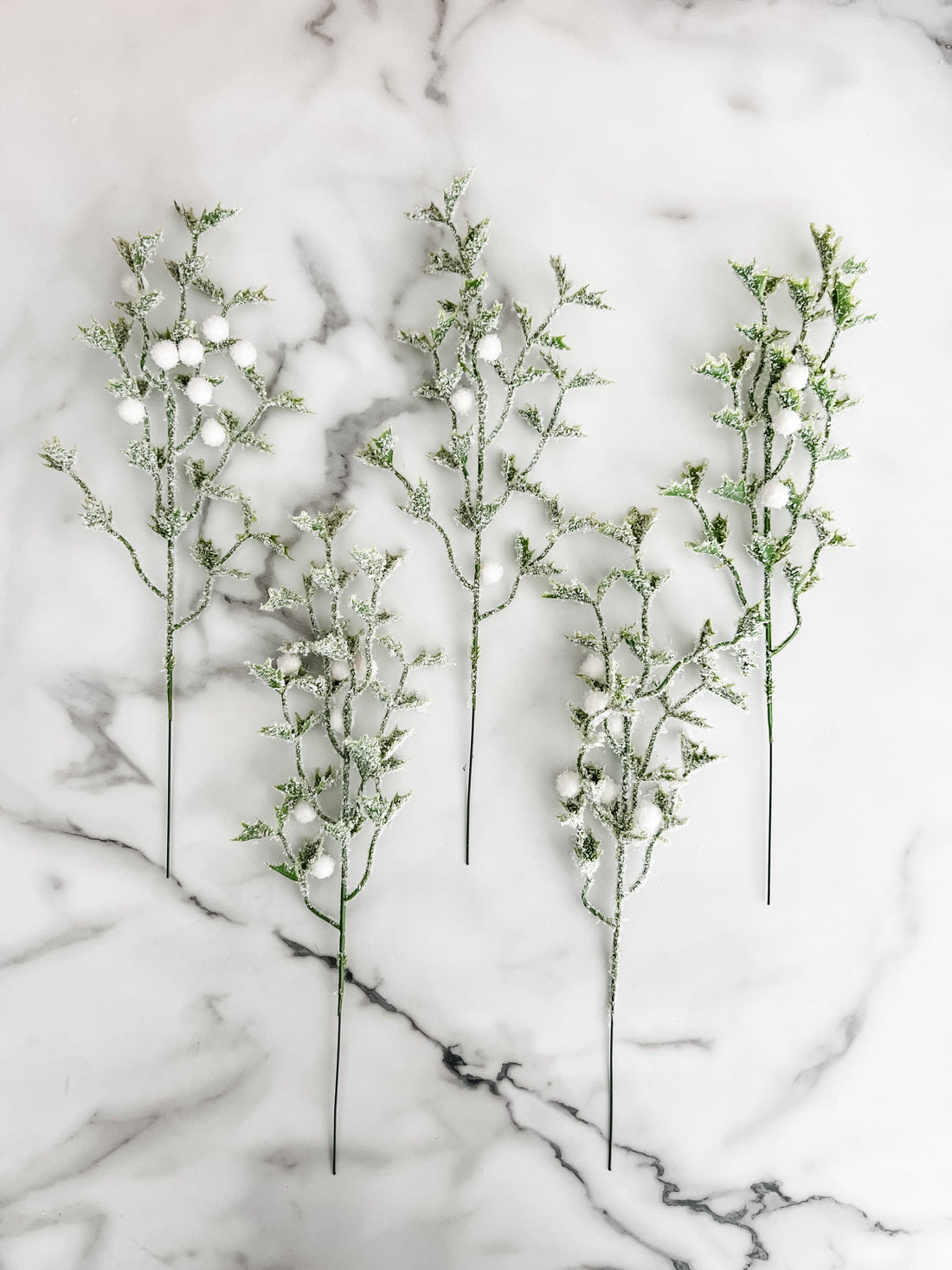 Set of decorative branches with small white berries on a marble surface
